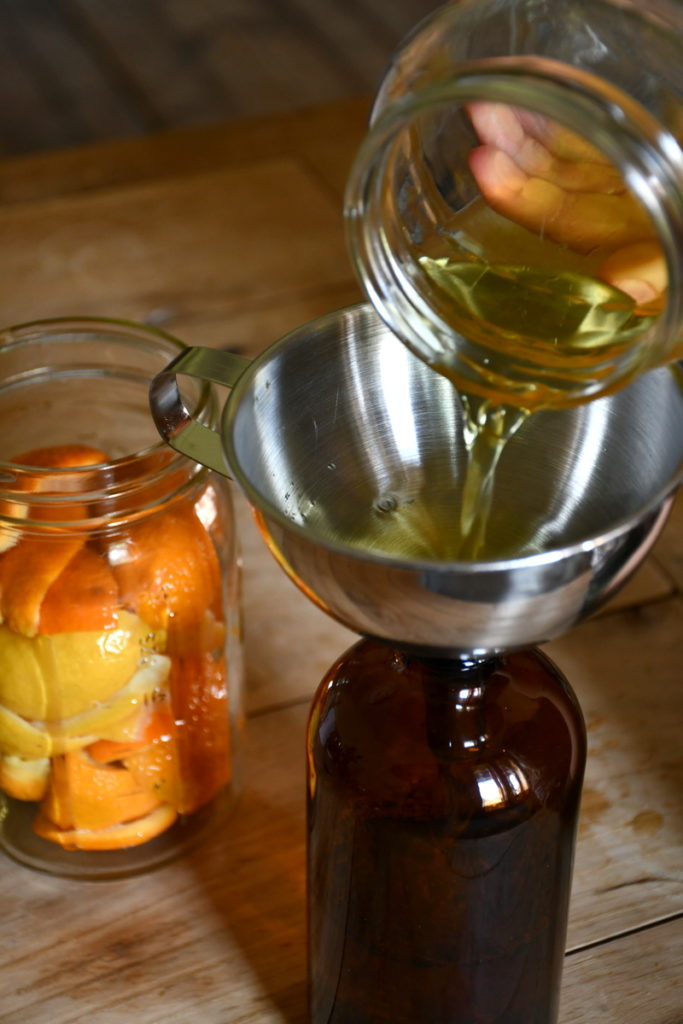An amber glass bottle has a metal funnel in the top and the newly made citrus cleaner is being poured into the jar.