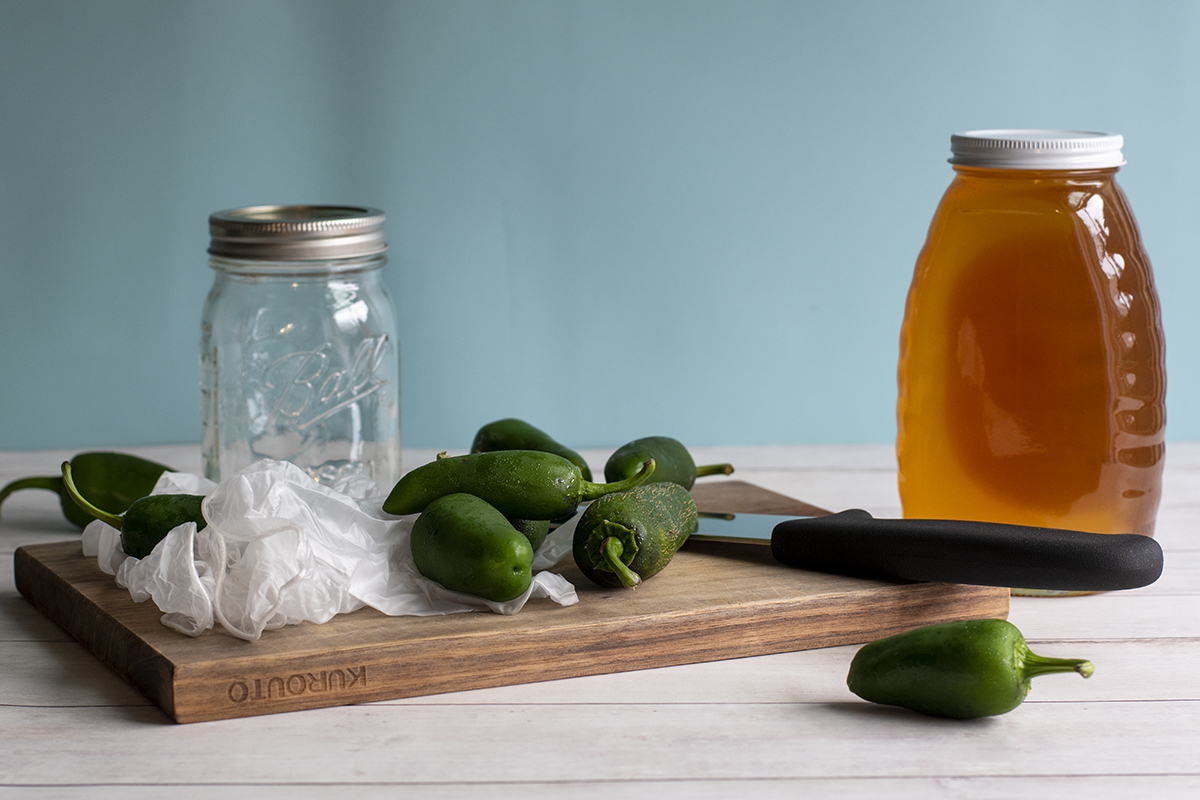 砧板，一罐蜂蜜，空玻璃瓶，一次性手套，厨师刀和新鲜的墨西哥胡椒