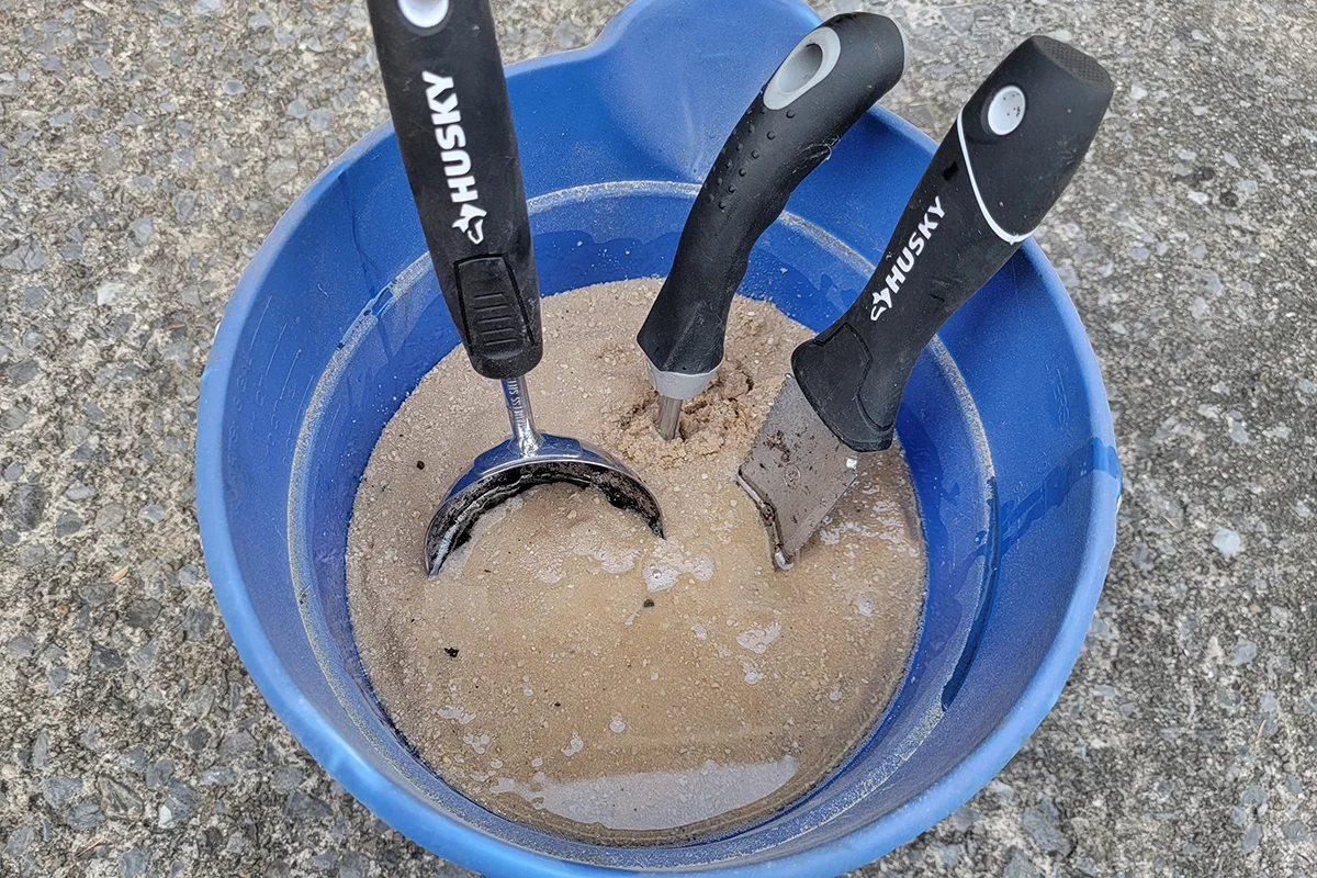 Blue bucket filled with sand and oil, garden tools immersed in sand