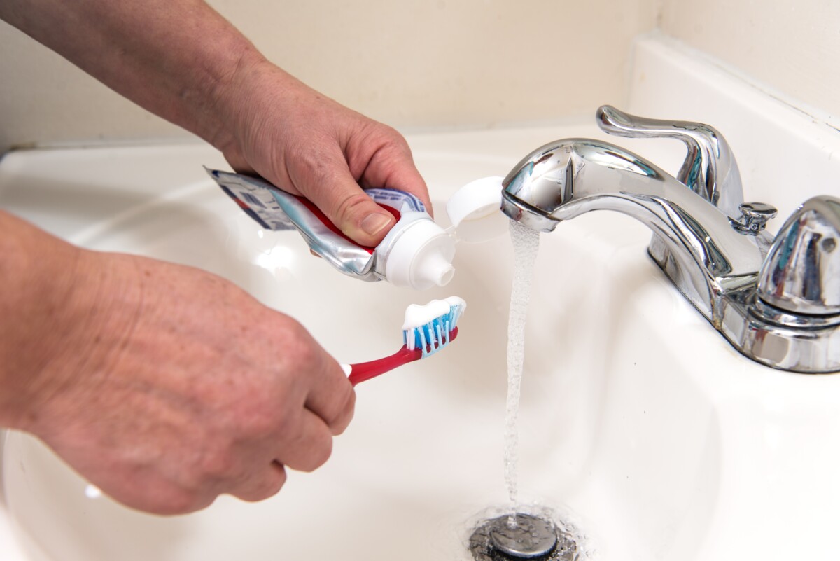 画面中，水从水龙头流出时，手正在往牙刷上涂牙膏。