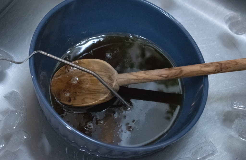 一碗热枫糖浆放在水槽里的冰浴里。一个木勺和一个数字温度计电极从糖浆中伸出来。