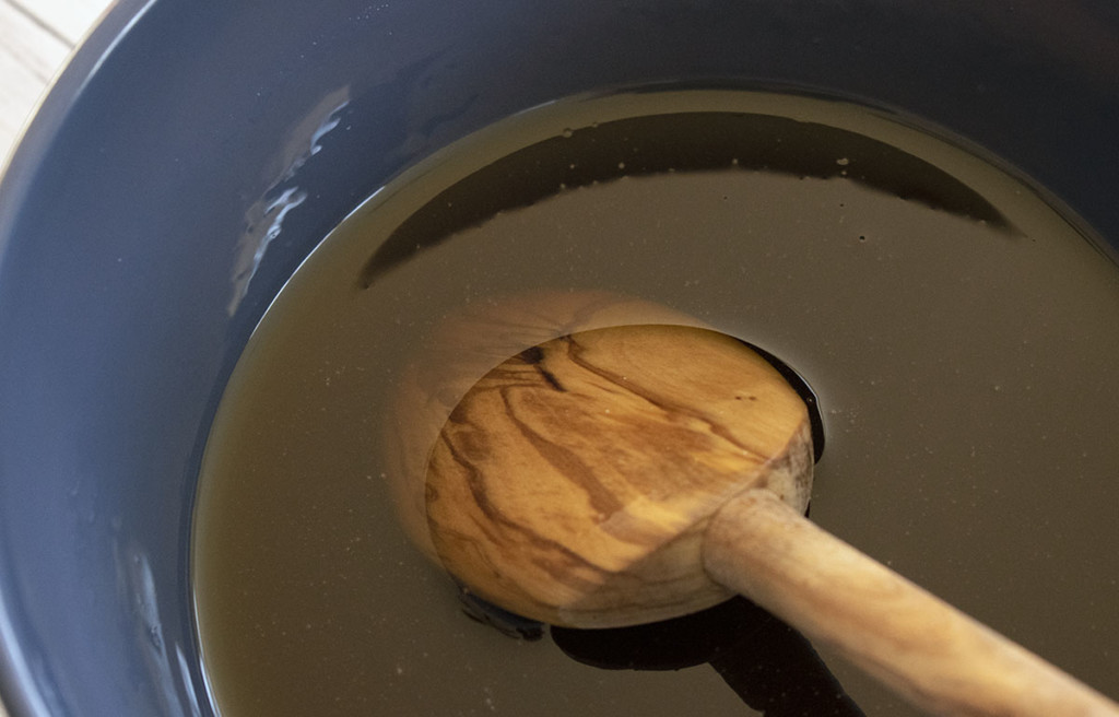 一个装有热枫糖浆的蓝色碗，它将被制成枫奶油。糖浆里有一把木勺。