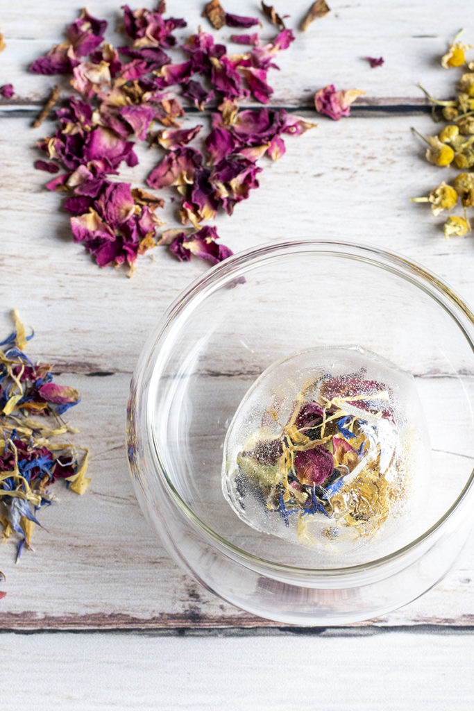 A tea bomb filled with floral tea in a clear glass tea cup with no water.